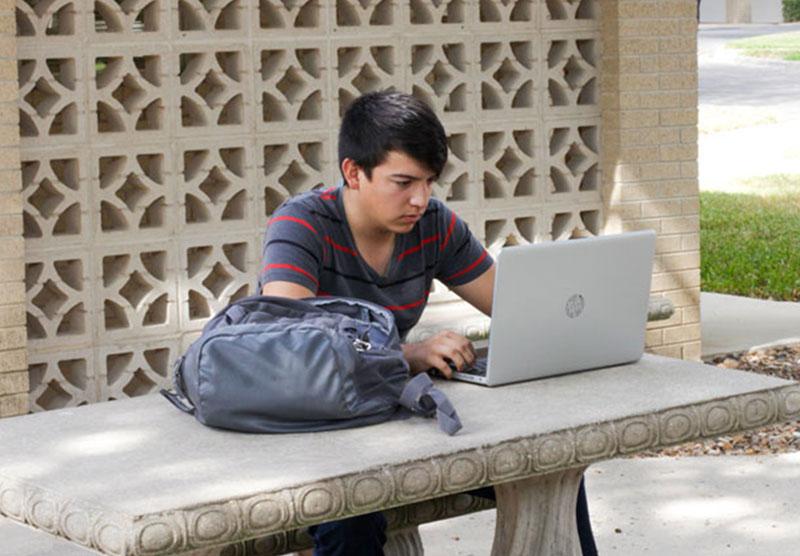 male student studying outdoors on a laptop